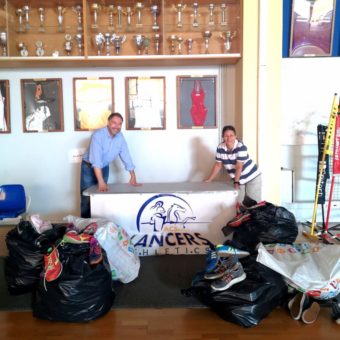 Mrs. Annie Constantinides, the ACS Athens Athletic Director and Mr. Kazantzopoulos, the President of the Institute Team of the World with the collected sports shoes.